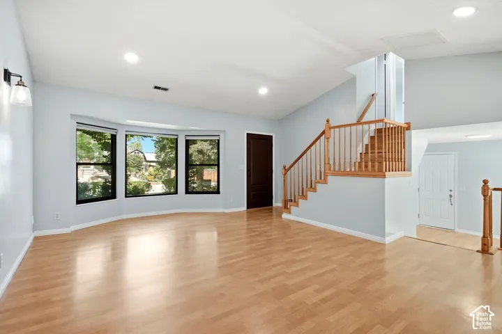 Spacious living area featuring wood-finish flooring, a bay window, recessed lighting, and a wood staircase