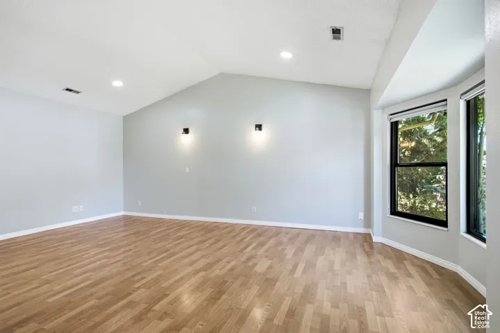 Vaulted ceiling with recessed lighting, wood-finish flooring, bay window with black frames, and wall-mounted sconces