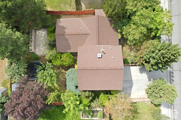 Aerial view showcasing a brick-exterior home with a multi-pitched roof and composite shingle roofing, surrounded by mature landscaping and established trees throughout the property