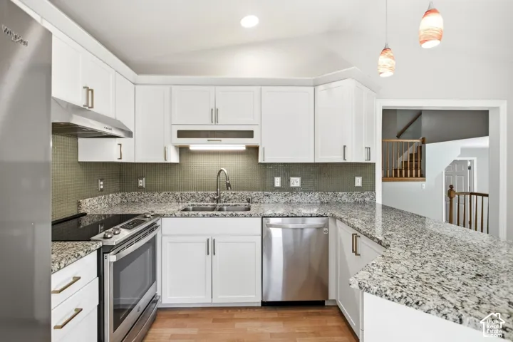 Kitchen featuring white cabinetry, light-toned countertops, a mosaic tile backsplash, stainless steel appliances, and a wood-finish floor