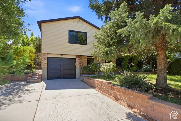 Multi-level residence featuring a one-car garage, concrete driveway, and brick retaining walls