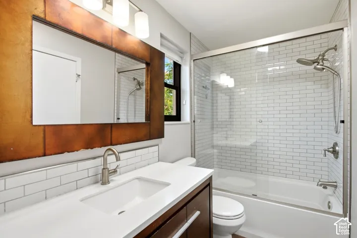 Main bathroom with entrance from hallway and master bedroom. Contemporary bathroom featuring a modern vanity with integrated sink, white subway tile backsplash, and a shower-over-tub combination with a sliding glass enclosure
