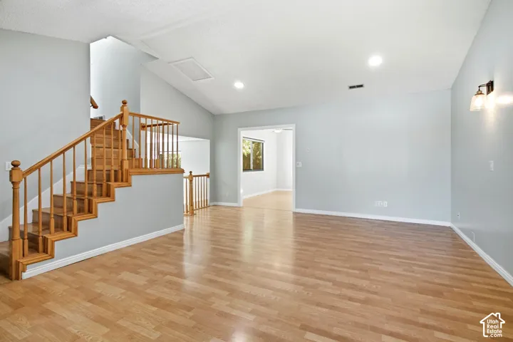 Vaulted ceiling, wood-finish flooring, natural wood staircase with balusters, and recessed ceiling lighting
