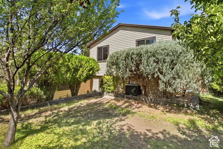 Siding exterior with multiple windows, surrounded by mature trees and shrubs