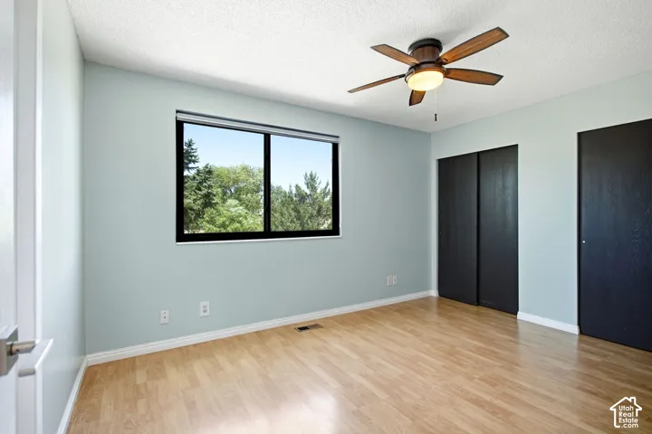 Master bedroom. Wood-finish flooring, full-light window, ceiling fan with integrated lighting, and black sliding closet doors