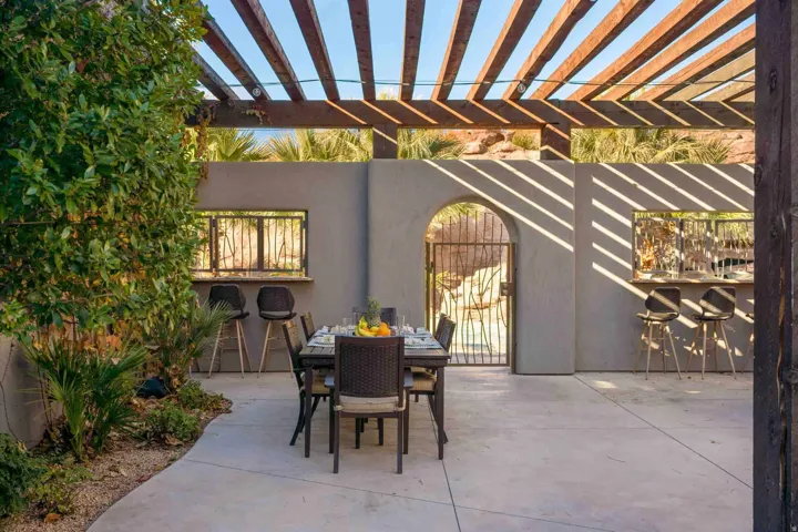 Spacious patio featuring a wood pergola, built-in bar, stucco walls, and an arched entryway with a decorative metal gate