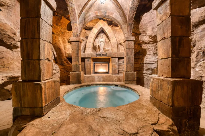 Spa with integrated waterfall feature, stone archways, sculptural details, recessed electric fireplace, and vaulted ceiling