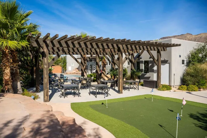 Wood pergola structure with concrete patio, artificial turf putting green, and mature palm trees