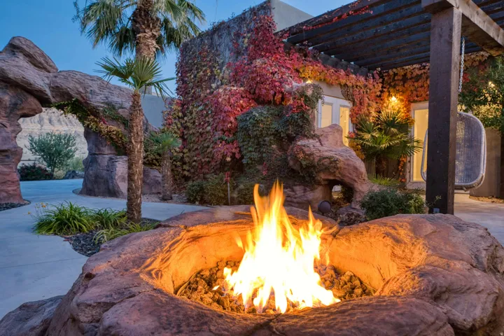 Rock-built fire pit, stone archway, extensive climbing foliage, mature palm trees, and a dark wood pergola