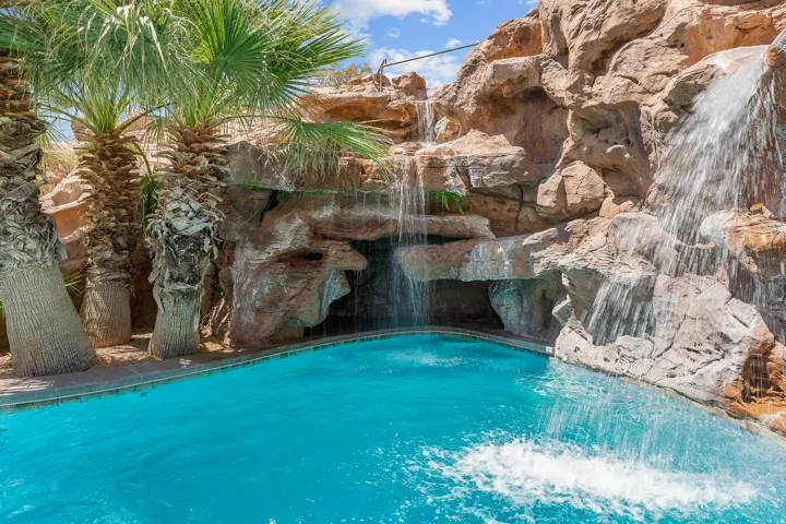 Swimming pool with a rock grotto, multiple waterfalls, and surrounding palm trees