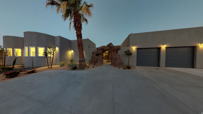 Modern stucco exterior with integrated exterior lighting, decorative rock archway, and two garage doors