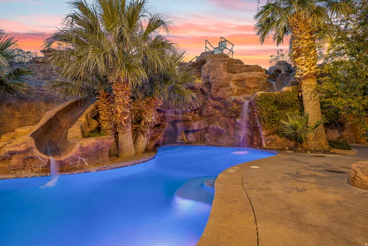 Freeform swimming pool with integrated rock features, illuminated waterfall, and a built-in water slide