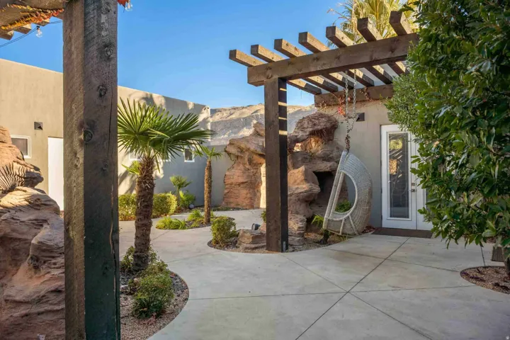 Outdoor patio with a wood pergola, expansive concrete hardscaping, and integrated rock features