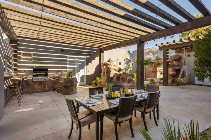 Expansive outdoor patio featuring a wooden pergola, built-in outdoor kitchen with grill, and custom rock landscaping
