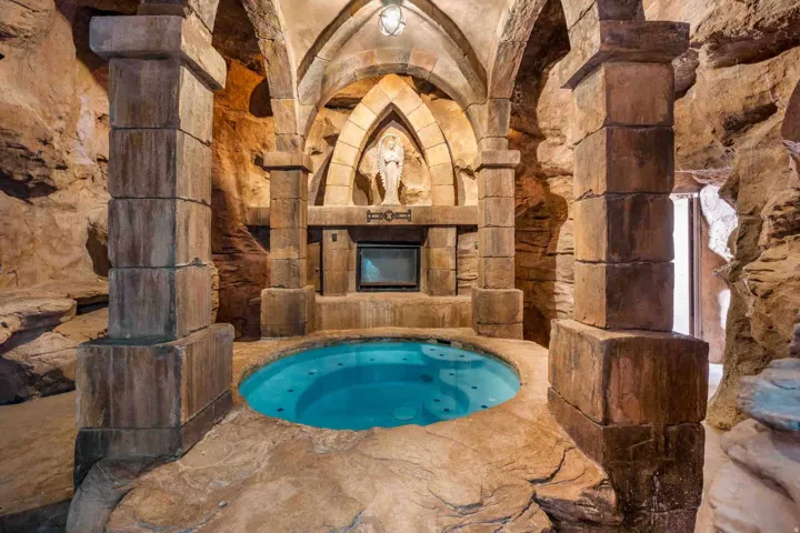 Sunken spa with a built-in television, archways, stone columns, and textured stone walls