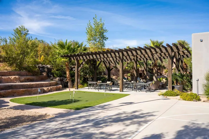 Expansive outdoor living area featuring a wooden pergola, a putting green, tiered rock landscaping, and mature palm trees