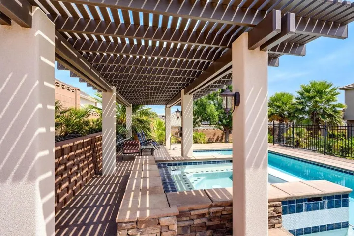 Expansive outdoor living area featuring a slatted pergola, integrated spa, and swimming pool