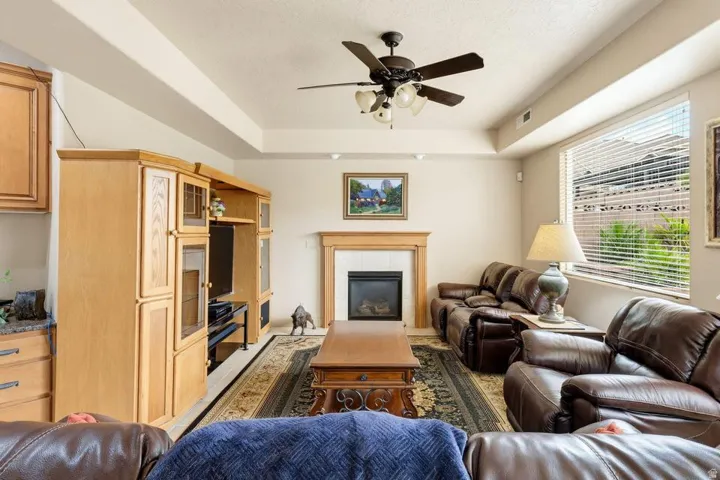 Spacious living room featuring vaulted ceilings with ceiling fan, built-in wood cabinetry and entertainment center, fireplace with wood mantel, large windows with blinds, and wood-finish flooring accented by area rug