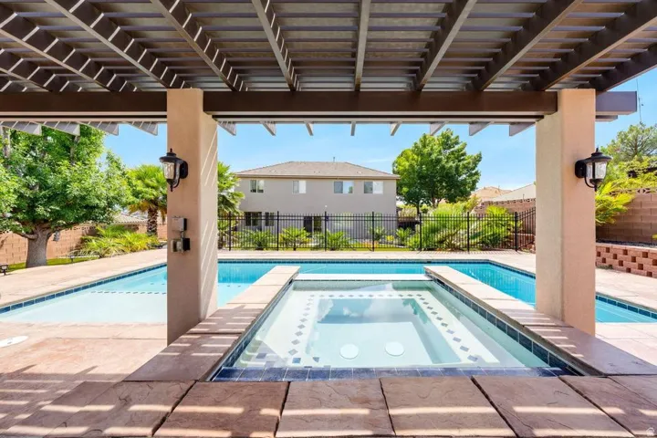 Pergola structure with integrated lighting, dual swimming pools, elevated spa with mosaic tile, and paver decking