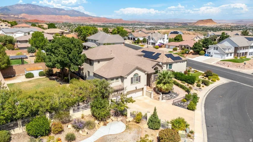 Multi-story residence featuring a tile roof, solar panels, a paved driveway, and established landscaping