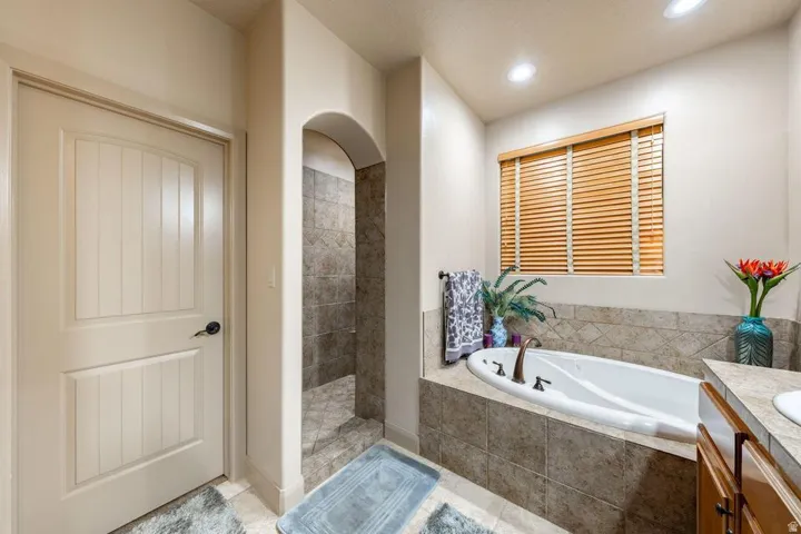 Soaking tub with bronze-finish fixtures, tile surround, and wood-finish blinds