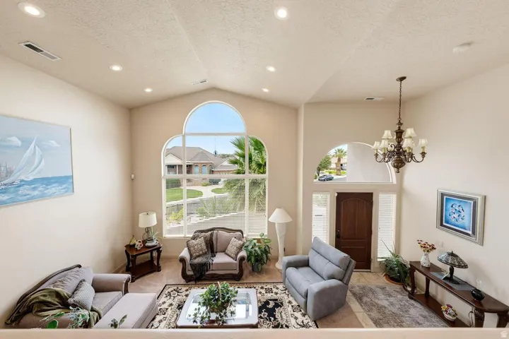 Vaulted ceiling with recessed lighting, large arched windows, dark wood entry door, and a multi-arm chandelier