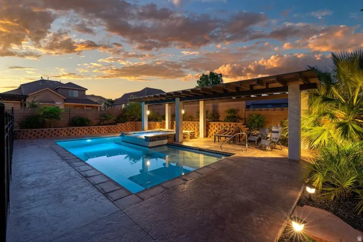 Swimming pool with integrated spa, stamped concrete decking, shaded pergola, and mature landscaping
