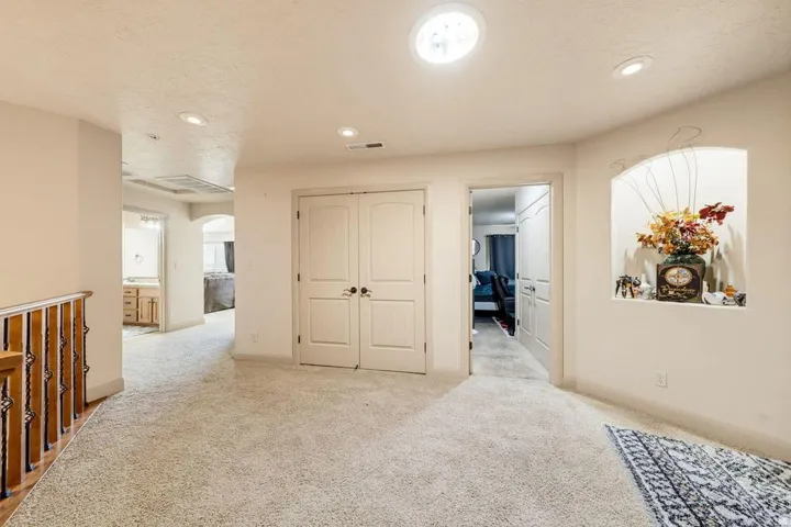 Carpeted flooring, recessed lighting, circular ceiling light fixture, arched wall niche, and panel doors with dark hardware