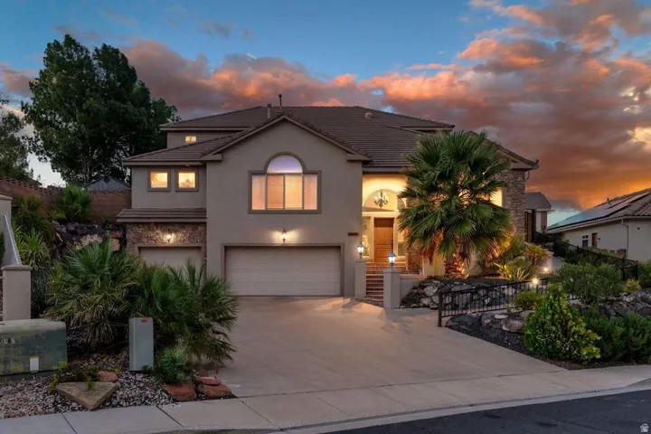 Stucco exterior with stone accents, arched entry, multiple garage bays, and integrated landscaping