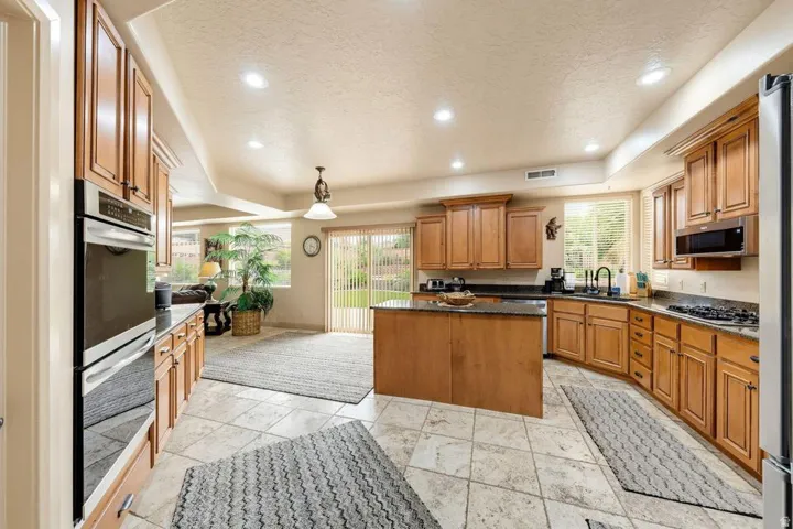 Kitchen featuring a central island, light wood cabinetry, stone-finish tile flooring, recessed lighting, and stainless steel built-in appliances
