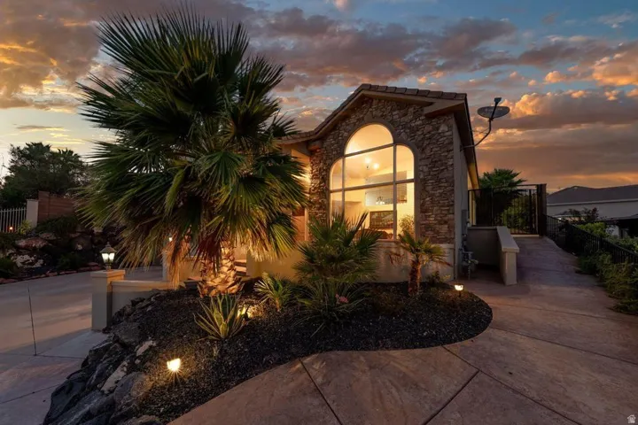 Stone facade exterior with an arched window, stamped concrete driveway, mature palm trees, and integrated landscape lighting