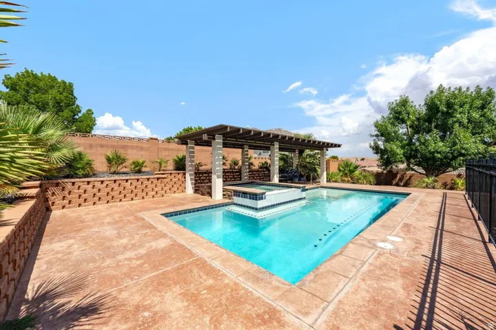 In-ground swimming pool featuring an integrated spa, an adjacent pergola, and a stamped concrete patio