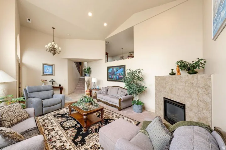 Vaulted ceilings with recessed lighting, floor-to-ceiling fireplace with tile surround, chandelier lighting, and an open entryway to a staircase
