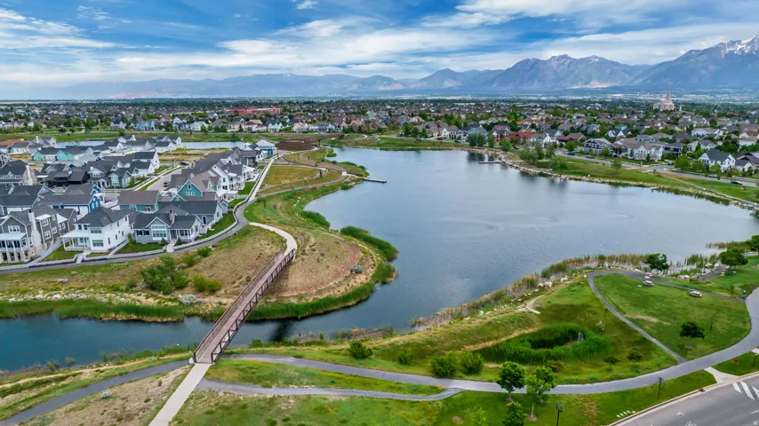 Expansive community featuring a large lake, residential homes, pedestrian bridge, paved walking paths, and distant mountains