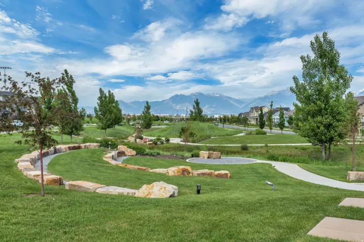 Expansive green space featuring a winding stone wall, paved pathways, mature trees, and landscaping