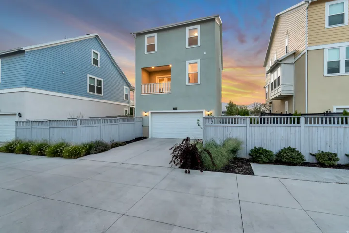 Three-story stucco exterior with a balcony, an attached garage, and a concrete driveway