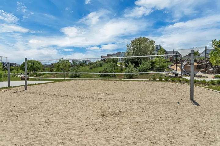 Sand volleyball court with a net, adjacent to a paved path and landscaped areas