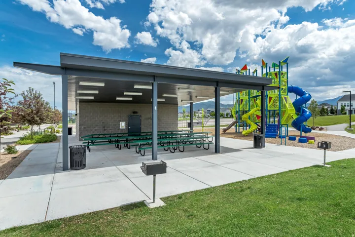 Covered picnic area with integrated lighting, multiple picnic tables, an adjacent playground structure, and a dedicated grilling station