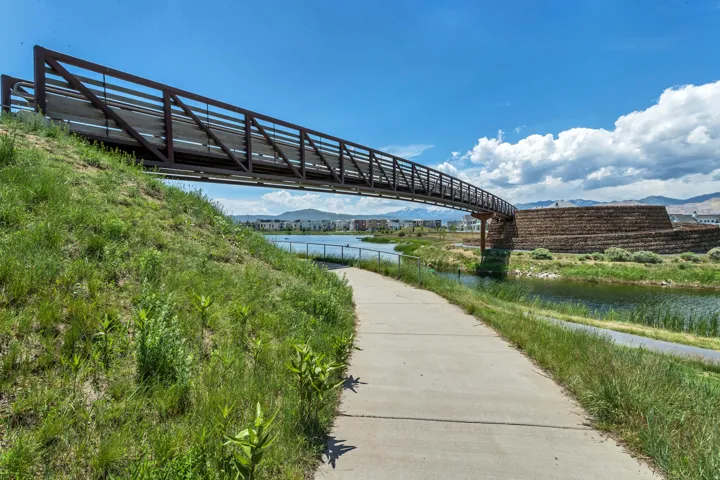 Concrete pathway alongside a body of water, featuring a pedestrian bridge and landscaped embankments