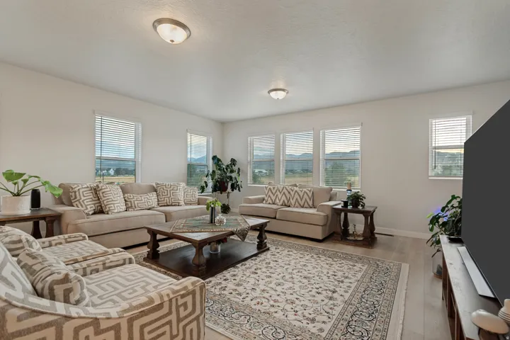 Spacious living area featuring light wood-finish flooring, multiple windows with blinds, and recessed lighting fixtures