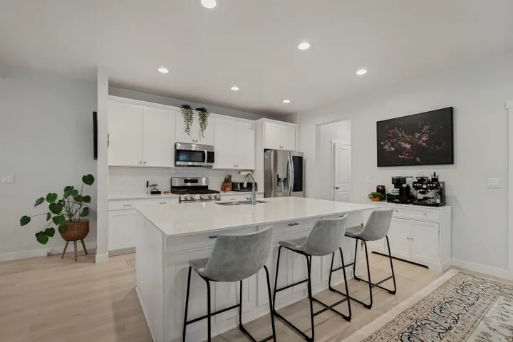 Stainless steel appliance suite, white shaker cabinetry, large center island with counter seating, subway tile backsplash, and light wood-finish flooring