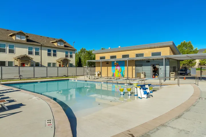 Community swimming pool with a shallow entry area, surrounding concrete deck, and adjacent building with covered patio
