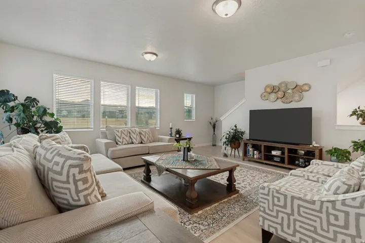 Spacious living area featuring light-colored walls, recessed lighting, wood-finish flooring, and multiple windows with blinds