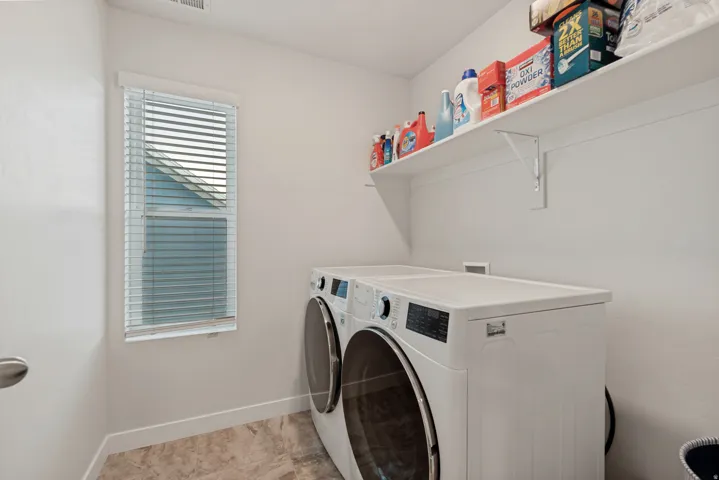 Functional laundry space featuring a window with blinds, durable tile flooring, and integrated wall shelving