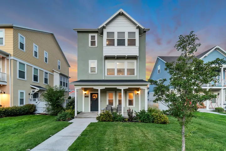 Three-story residence featuring a covered front porch, stucco and horizontal siding exterior, and a manicured lawn