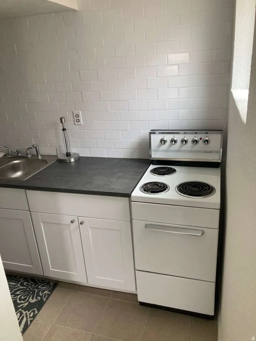 White subway tile backsplash, dark countertop, stainless steel sink, white cabinetry with silver hardware, and a white electric range