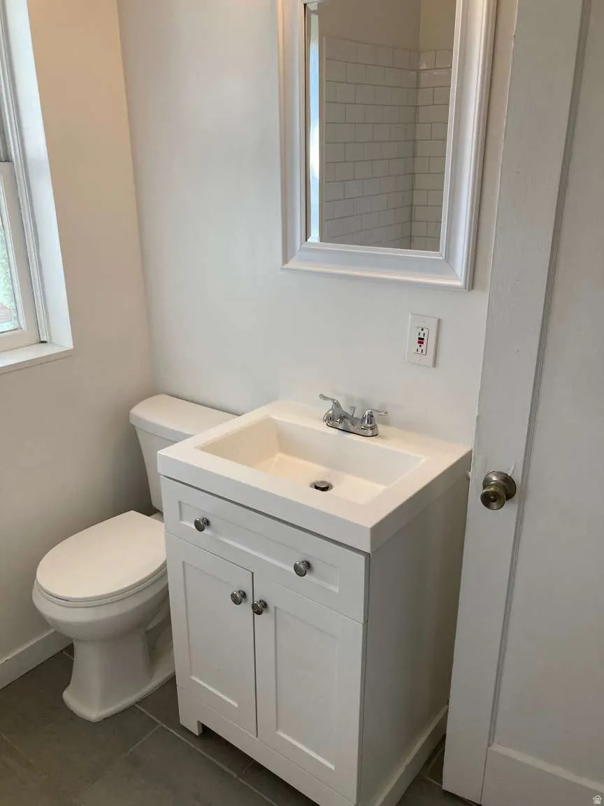 White vanity with integrated sink, chrome faucet, framed mirror, and subway tile shower visible in reflection