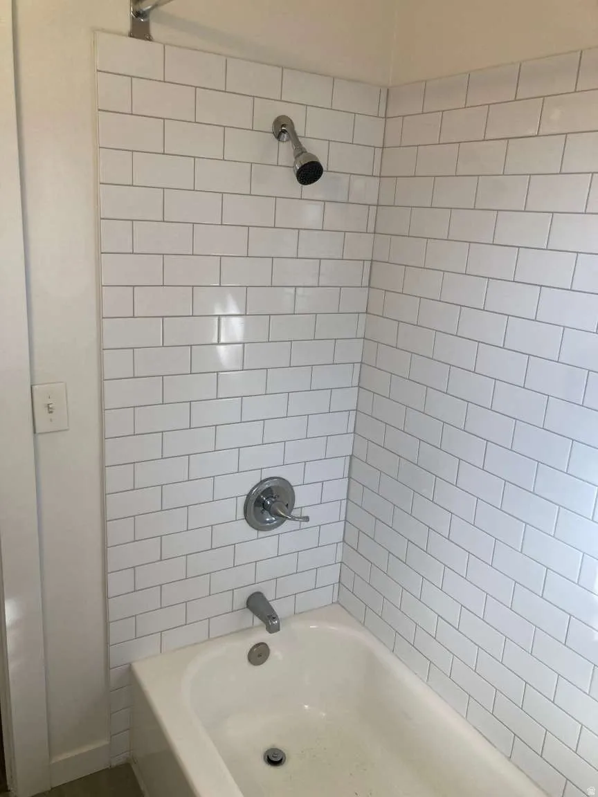 Bathtub with white subway tile surround, chrome shower head, and chrome bath fixtures