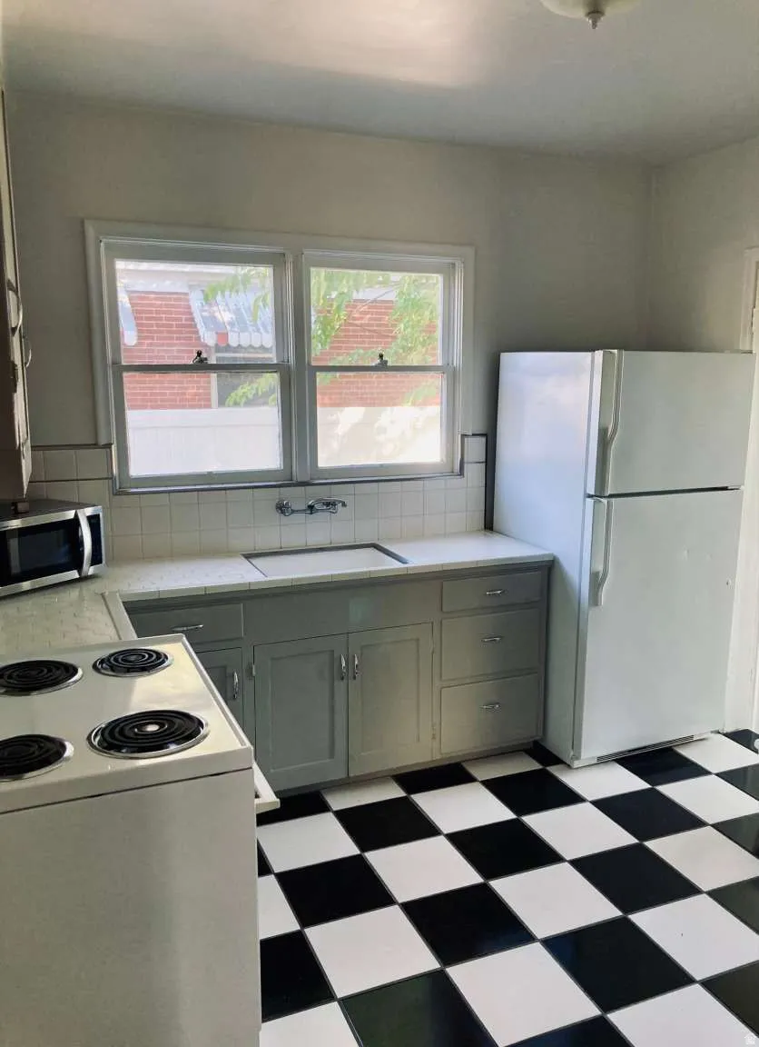 Kitchen featuring checkerboard flooring, white tile backsplash, a double window, and gray base cabinetry with metal pulls
