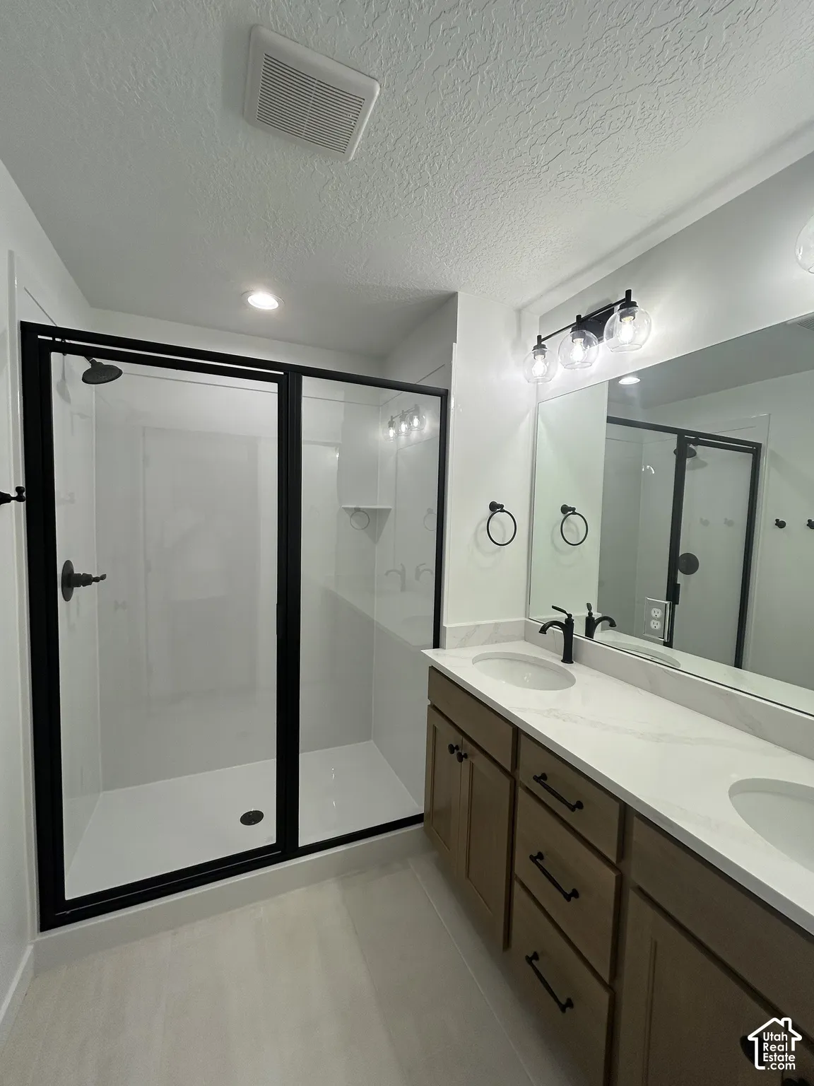 Walk-in shower with black-framed glass enclosure, double vanity with integrated sinks, wood-finish cabinetry, and contemporary black fixtures